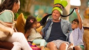 Family with 2 young children playfully tugging on the father’s Goofy hat