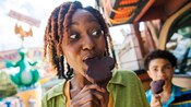 A woman and her son eating Mickey ice cream bars outside at a theme park