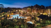 Alpine trees surrounding a multistory wood and stone wilderness lodge with an impressive pool area 