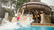 A girl slides into a pool with a large splash
