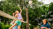 A man holds his daughter up to spike a volleyball over a net