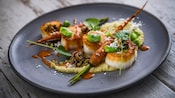 Four scallops drizzled with sauces served with hummus and a long, roasted carrot