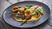 Four scallops drizzled with sauces served with hummus and a long, roasted carrot