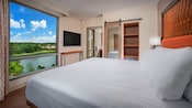 Una ventana con vista, consola, TV, baño, armario, una cama y una mesa lateral con lámpara