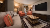 Una habitación con un sofá, 2 sillas, 2 lámparas, una mesa ratona, cajones y una pantalla de TV