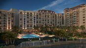 3 massive wings of Disney's Riviera Resort loom behind a large swimming pool lined with palm trees