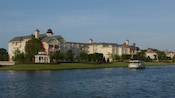 An open aired riverboat sailing alongside the Victorian style Disney's Saratoga Springs Resort and Spa