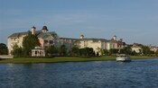 An open aired riverboat sailing alongside the Victorian style Disney's Saratoga Springs Resort and Spa