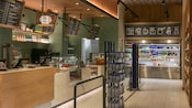 Una cafetería contemporánea con una zona de pedidos en el mostrador y una vitrina refrigerada con bebidas y snacks para llevar.