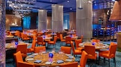 A modern restaurant with formally set tables, booths, decorative columns and abstract chandeliers that resemble underwater bubbles