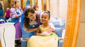 Uma cabeleireira sorri com uma menina vestida de princesa em um ambiente de salão de beleza