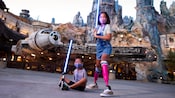 A young woman holding a lightsaber in her hands and a young boy holding a lightsaber between his feet in Star Wars Galaxy's Edge