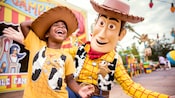 A young boy wearing a Woody themed tee shirt and cowboy hat laughs as a interacts with Woody inside of Toy Story Land A young boy wearing a Woody themed tee shirt and cowboy hat laughs as a interacts with Woody inside of Toy Story Land