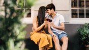 A young couple nuzzles on bench while holding glasses of wine A young couple nuzzles on bench while holding glasses of wine