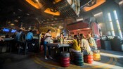 A woman hands food to her family, seated inside a Star Wars cargo building where large containers of food are lowered from the ceiling