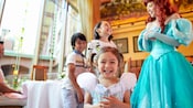A little girl beams as her brother and sister share a laugh with Princess Ariel in the background