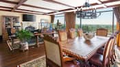 A long wooden dining table with a rustic chandelier overhead, next to a window