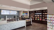 The hotel convenience store features a service counter, refrigerated cases, freestanding racks and shelving units filled with boxed meals, snacks and beverages