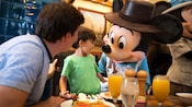 Mickey greets a young boy and his Dad at their breakfast table Mickey greets a young boy and his Dad at their breakfast table