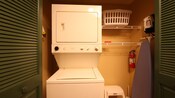 Stacked washer and dryer next to shelves and laundry basket