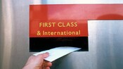 A hand putting a letter into a First Class & International mail slot