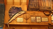 A wood-paneled wall with a stuffed swordfish, fish pictures, a net and fishing boat gear
