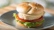 A grilled chicken breast on a bun with lettuce, tomato and cheese