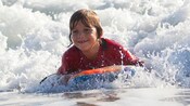 A smiling boy rides a bodyboard in low surf