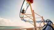 A Guest watersliding through a translucent tube extended over the side of the ship overlooking the ocean