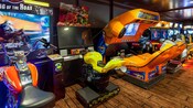 En una sala de videojuegos, 2 videojuegos con asientos que se asemejan a una motocicleta, junto a videojuegos de alta tecnología