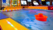 En una sala de videojuegos, un tablero de hockey de mesa rodeado por una gran variedad de videojuegos de alta tecnología