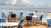 Chairs and round tables on a Disney Cruise Line deck with a railing overlooking the ocean