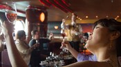 A woman looks at a drink in her glass in a room full of people also looking at their drinks