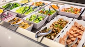 A salad bar that includes lettuce, tomatoes, peppers, cucumbers, meats and prepared vegetable mixtures