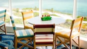 By a wall of windows, 4 striped chairs at a table with salt, pepper and cutlery in a wire basket