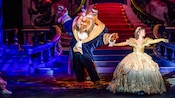 The Beast dances with Belle in front of a grand staircase