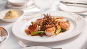 Quinoa with vegetables on top, surrounded by 5 grilled scallops and asparagus in a delicate sauce