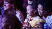 A smiling mother and her young daughter sit among other engaged audience members watching a live performance at the Walt Disney Theatre.
