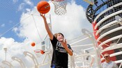 A young boy jumping up toward the top of a basketball hoop to dunk a basketball while father watches on