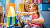 A Cast Member reads a book to a little girl, at Its a Small World Nursery on the Disney Dream
