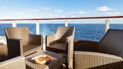 Three wicker chairs and a wicker table sit on a deck with an ocean view