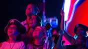 A family at night dressed in Pirates of the Caribbean garb look up to the night sky lit by fireworks