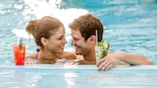 A young couple relaxing at the edge of the pool sipping refreshing drinks