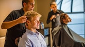 A hairdresser provides haircutting consultation to a young man seated at his station