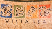 Small tiled mosaic depicting a bird, a flower, a face and some fruit with the words Vista Spa underneath
