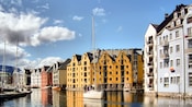 Identical 6-story houses and a marina line the waterways of a canal while a sailboat coasts between them