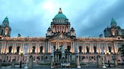 People walk near a large building with a statue in front of it