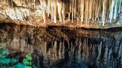 Stalactites hang over a pool of water in a cave