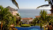 Palm trees frame a view of a villa overlooking a beach that stretches toward the horizon