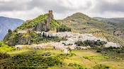 A village on a grassy hill with old ruins at the top